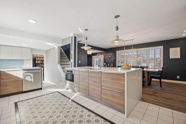 kitchen featuring light tile patterned flooring, appliances with stainless steel finishes, decorative light fixtures, sink, and white cabinets