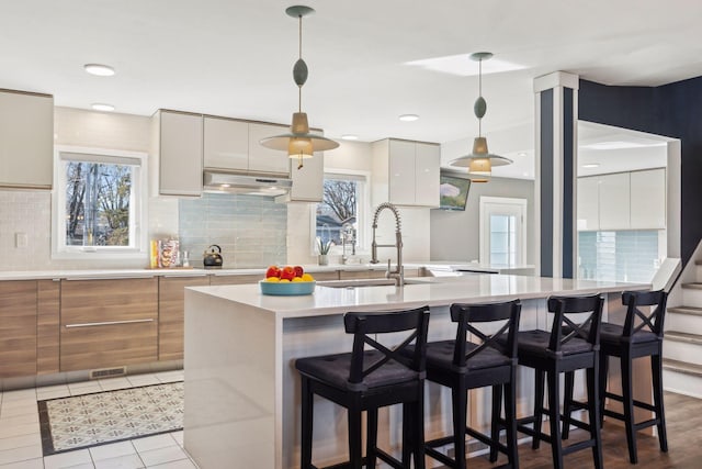 kitchen with sink, a center island with sink, decorative backsplash, and decorative light fixtures