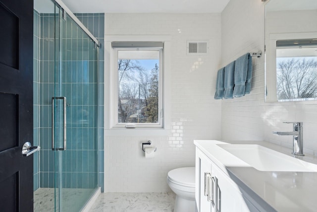 bathroom with tile walls, vanity, toilet, and an enclosed shower