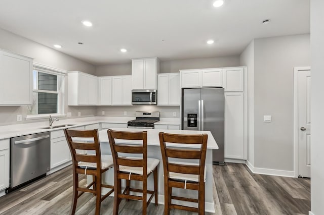 kitchen with appliances with stainless steel finishes, dark hardwood / wood-style flooring, sink, white cabinets, and a center island