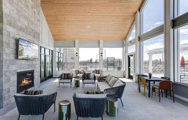 sunroom / solarium with a healthy amount of sunlight, wooden ceiling, an outdoor stone fireplace, lofted ceiling, and a water view