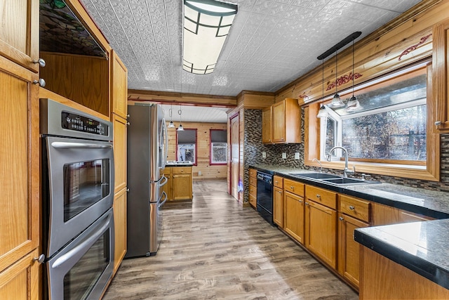 kitchen featuring hanging light fixtures, sink, hardwood / wood-style floors, wooden walls, and stainless steel appliances