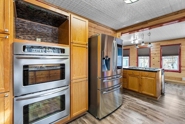 kitchen with stainless steel appliances, wood walls, wood-type flooring, and decorative light fixtures