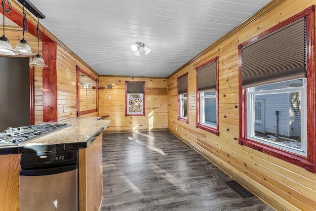 interior space with stainless steel gas stovetop, dark stone countertops, pendant lighting, dark hardwood / wood-style flooring, and wood walls