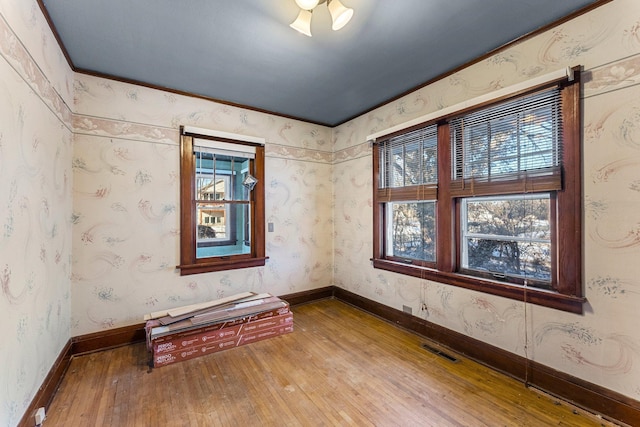 spare room featuring wood-type flooring, a healthy amount of sunlight, and ornamental molding