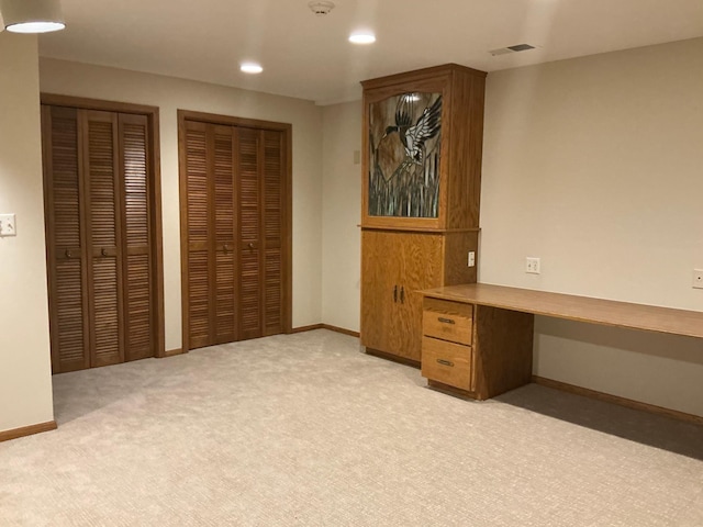 unfurnished office featuring built in desk and light colored carpet