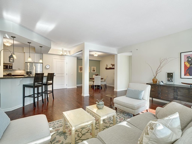 living area featuring a notable chandelier, dark wood finished floors, and baseboards