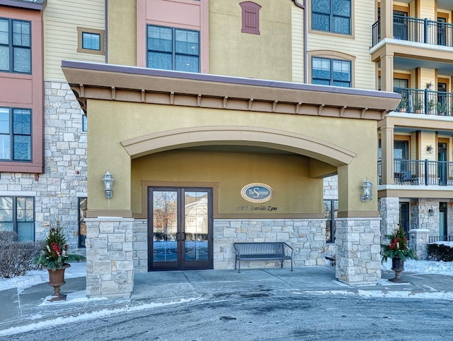 property entrance with stucco siding, stone siding, and french doors