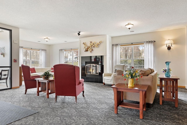 living room featuring plenty of natural light, dark carpet, a fireplace, and a textured ceiling