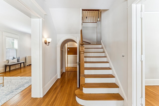 stairway with arched walkways, radiator heating unit, baseboards, and hardwood / wood-style floors