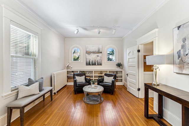 sitting room with crown molding, radiator heating unit, a healthy amount of sunlight, and light wood finished floors