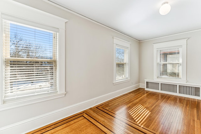 spare room with baseboards, radiator, ornamental molding, and hardwood / wood-style flooring