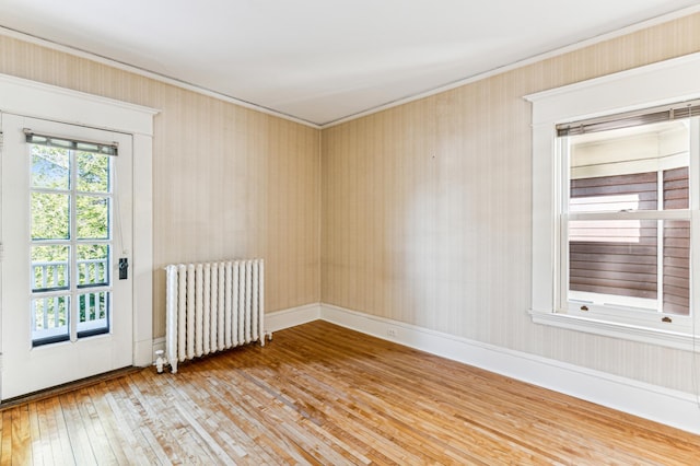 empty room featuring baseboards, wood-type flooring, radiator, and crown molding