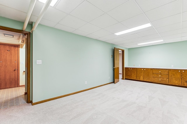 spare room featuring a drop ceiling, baseboards, and light colored carpet