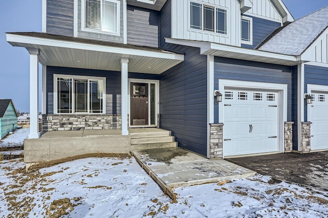 snow covered property entrance with covered porch and a garage