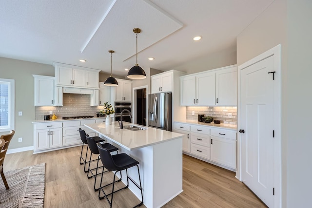 kitchen with white cabinets, appliances with stainless steel finishes, a kitchen bar, an island with sink, and hanging light fixtures