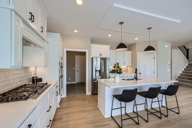 kitchen featuring white cabinetry, stainless steel appliances, tasteful backsplash, a kitchen island with sink, and light wood-type flooring