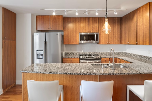 kitchen featuring pendant lighting, sink, stone counters, appliances with stainless steel finishes, and light wood-type flooring