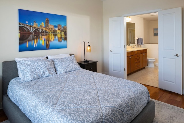 bedroom with ensuite bathroom, sink, and light hardwood / wood-style flooring