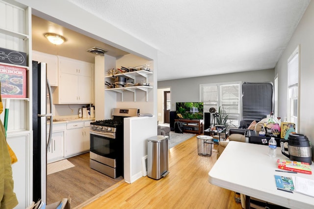 kitchen featuring light wood-type flooring, a textured ceiling, stainless steel appliances, and white cabinetry