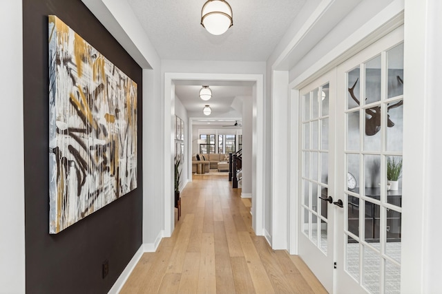 hallway with french doors, light hardwood / wood-style floors, and a textured ceiling