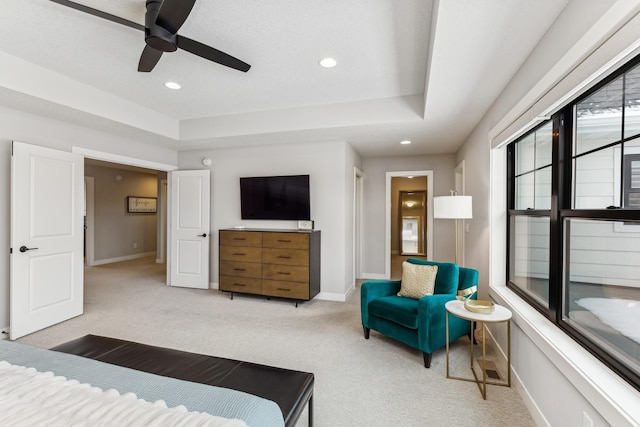 bedroom featuring a raised ceiling, light carpet, and ceiling fan