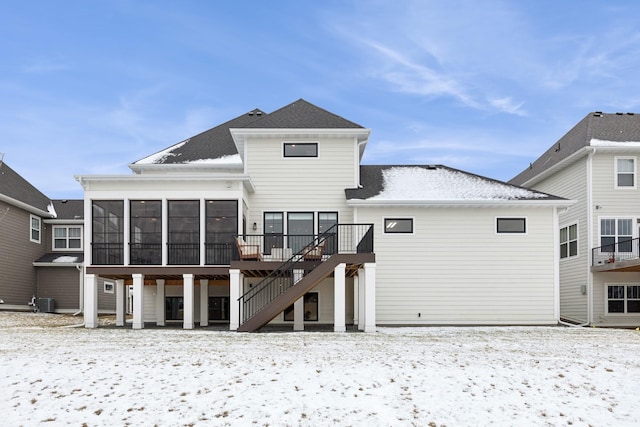 snow covered rear of property featuring a sunroom and a deck