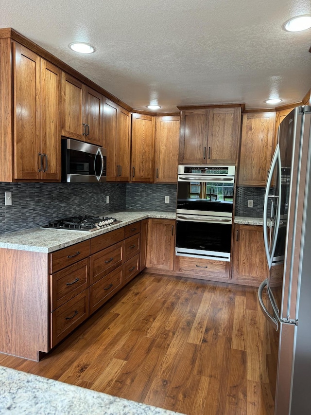 310 7th St SW, Roseau, MN 56751 - kitchen with a textured ceiling, brown cabinets, tasteful backsplash, appliances with stainless steel finishes, and dark wood-type flooring