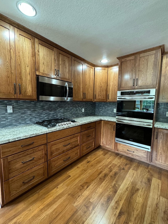 310 7th St SW, Roseau, MN 56751 - kitchen featuring a textured ceiling, tasteful backsplash, brown cabinets, light wood-style flooring, and stainless steel appliances