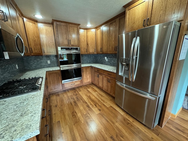 310 7th St SW, Roseau, MN 56751 - kitchen featuring light wood-style flooring, stainless steel appliances, recessed lighting, brown cabinetry, and backsplash