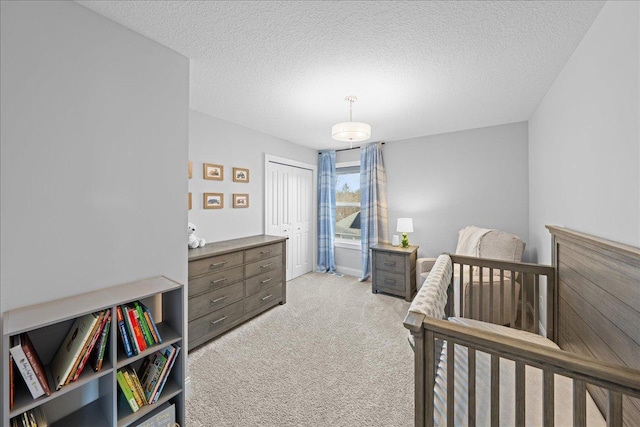 bedroom with a nursery area, light colored carpet, a textured ceiling, and a closet