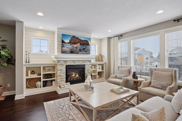 living area with dark wood-type flooring, baseboards, a stone fireplace, and a textured ceiling