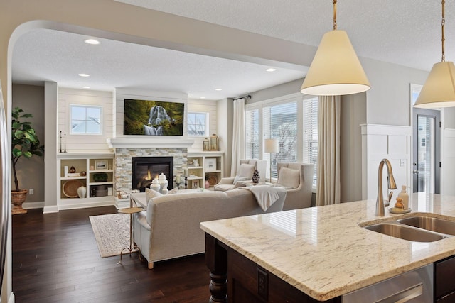 living room featuring a textured ceiling, a stone fireplace, recessed lighting, dark wood-style flooring, and baseboards