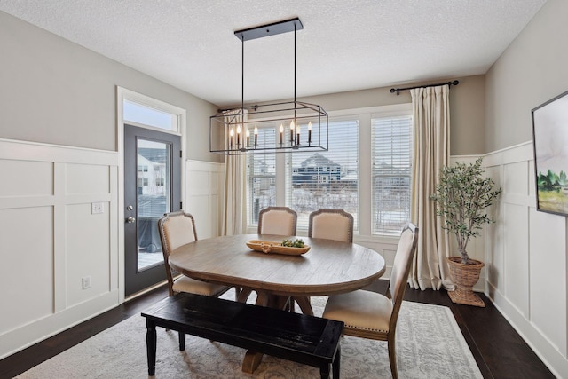 dining space with a textured ceiling, a decorative wall, a wainscoted wall, dark wood-type flooring, and an inviting chandelier