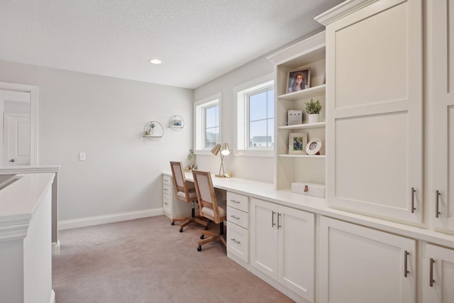 office area featuring a textured ceiling, baseboards, and light colored carpet