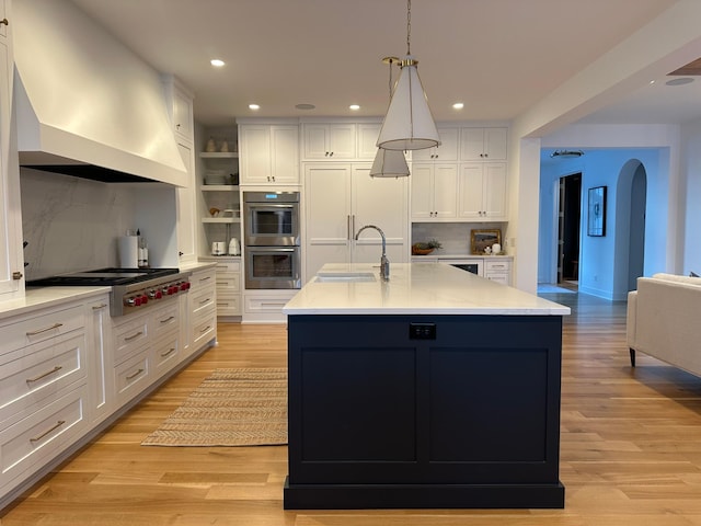 kitchen with appliances with stainless steel finishes, white cabinetry, an island with sink, sink, and custom range hood