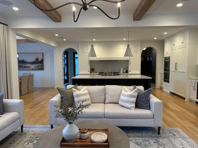 living room with beam ceiling, sink, light hardwood / wood-style flooring, and a notable chandelier