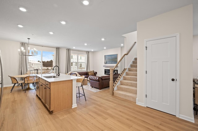 kitchen featuring pendant lighting, sink, light hardwood / wood-style flooring, an island with sink, and a chandelier