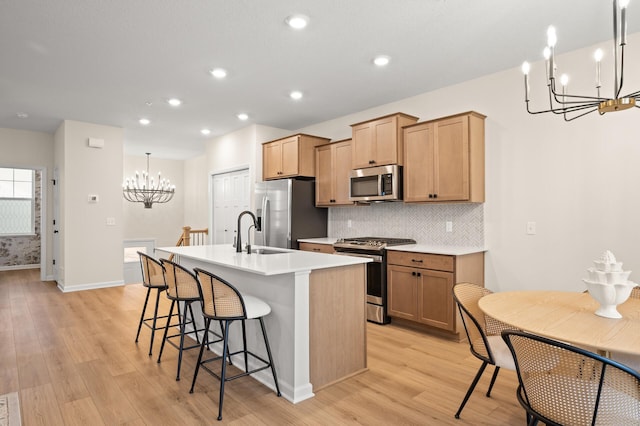 kitchen featuring appliances with stainless steel finishes, an island with sink, sink, hanging light fixtures, and light hardwood / wood-style floors