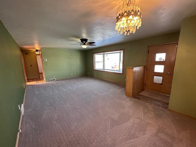 unfurnished living room with carpet flooring and ceiling fan with notable chandelier