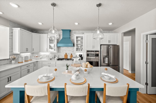 kitchen featuring a kitchen island, premium range hood, decorative light fixtures, and appliances with stainless steel finishes