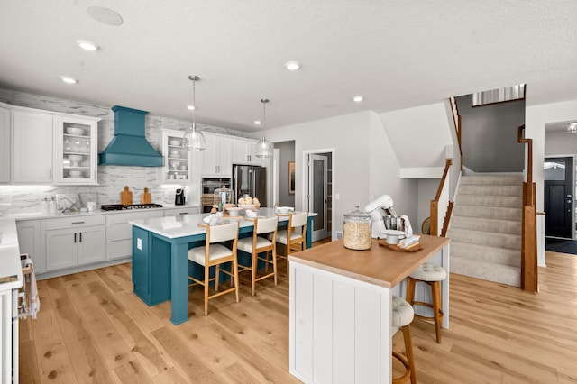 kitchen with white cabinets, appliances with stainless steel finishes, a kitchen island, decorative light fixtures, and custom range hood