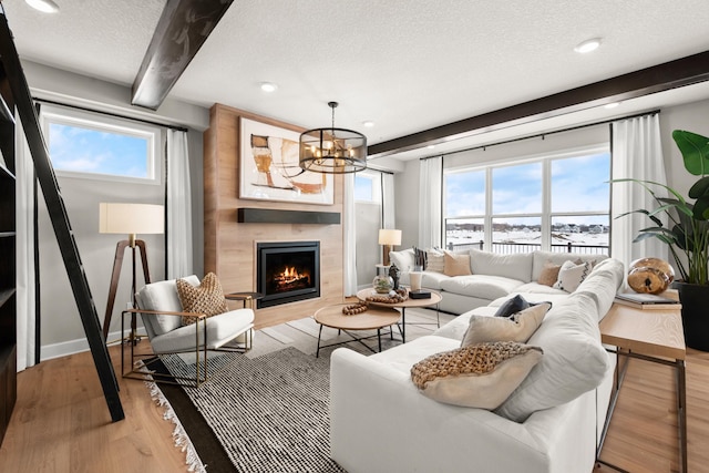 living room featuring a textured ceiling, beamed ceiling, light hardwood / wood-style floors, a large fireplace, and a chandelier