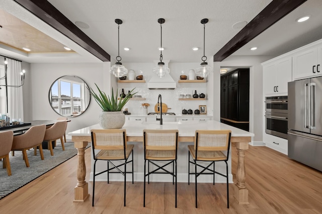 kitchen featuring a kitchen breakfast bar, appliances with stainless steel finishes, beam ceiling, and white cabinetry