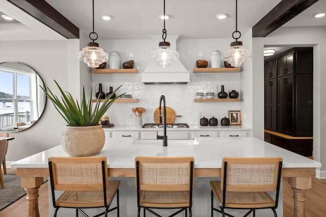 bar with backsplash, premium range hood, light hardwood / wood-style flooring, hanging light fixtures, and stainless steel gas cooktop