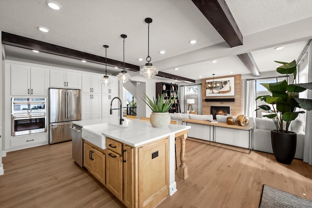 kitchen with an island with sink, appliances with stainless steel finishes, beam ceiling, white cabinets, and sink