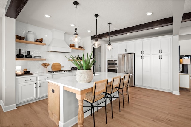 kitchen featuring premium range hood, a breakfast bar area, stainless steel appliances, white cabinets, and beamed ceiling