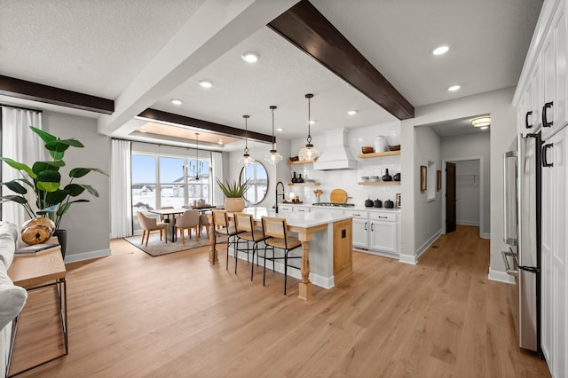 kitchen with white cabinetry, an island with sink, a kitchen breakfast bar, custom range hood, and beam ceiling