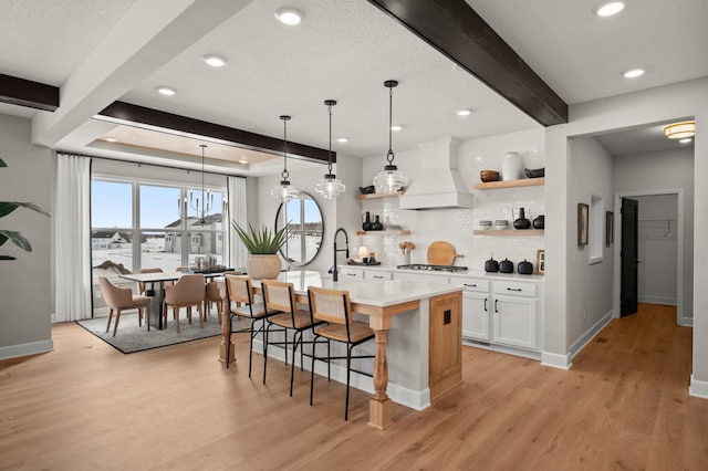 kitchen with white cabinets, an island with sink, premium range hood, beam ceiling, and a breakfast bar area