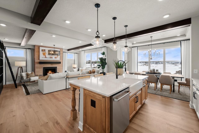 kitchen with a fireplace, stainless steel dishwasher, a center island with sink, and decorative light fixtures